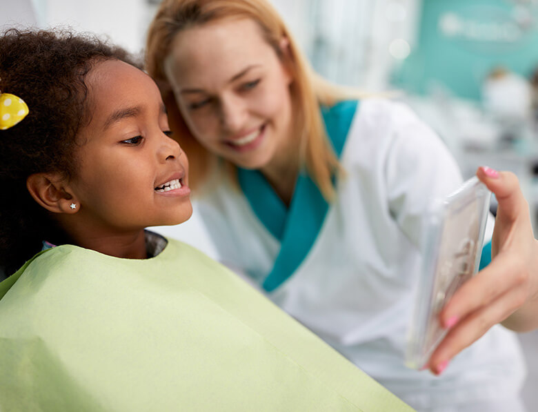 dental hygienist holding a mirror up for young patient to see her bright smile